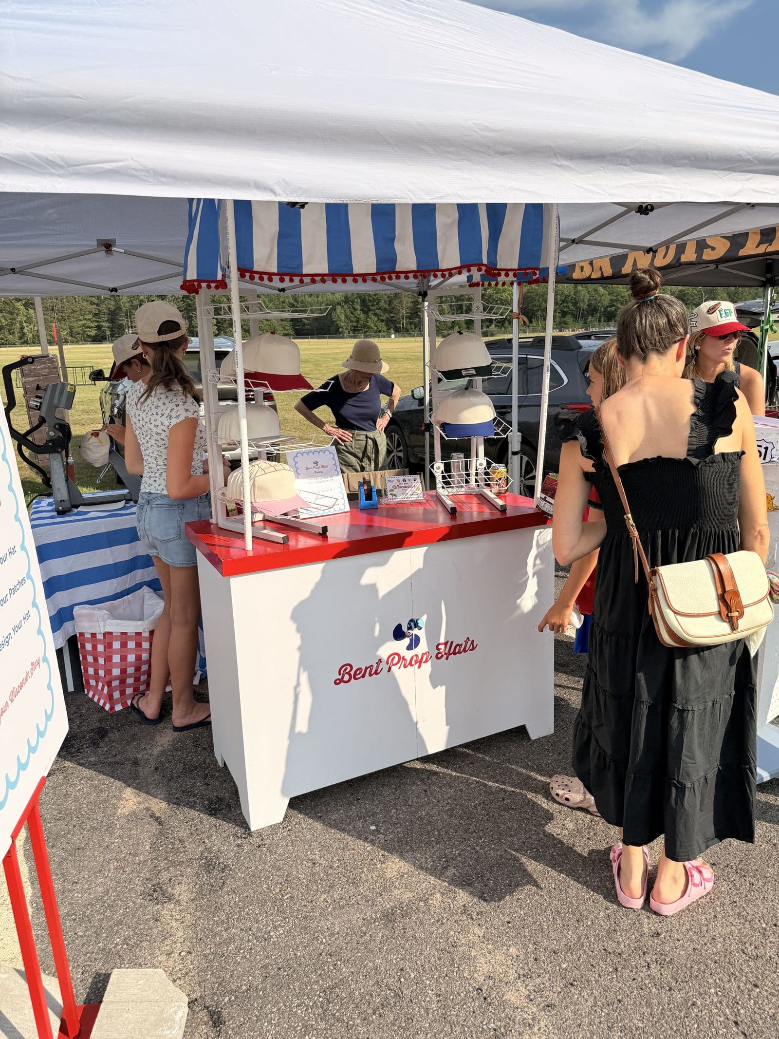 Shoppers at the Bent Prop Hats cart under the market tent